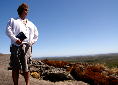 vorne links sitzt ein junger Mann mit dem GöTe in der Hand auf einem Felsen im Hintergrund ist eine Weitansicht von South Australia