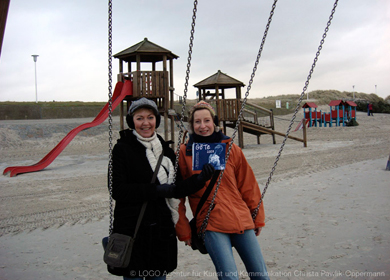 zwei frauen auf einer Schaukel halten den GöTe hoch im Hintergrund ein Spielplatz